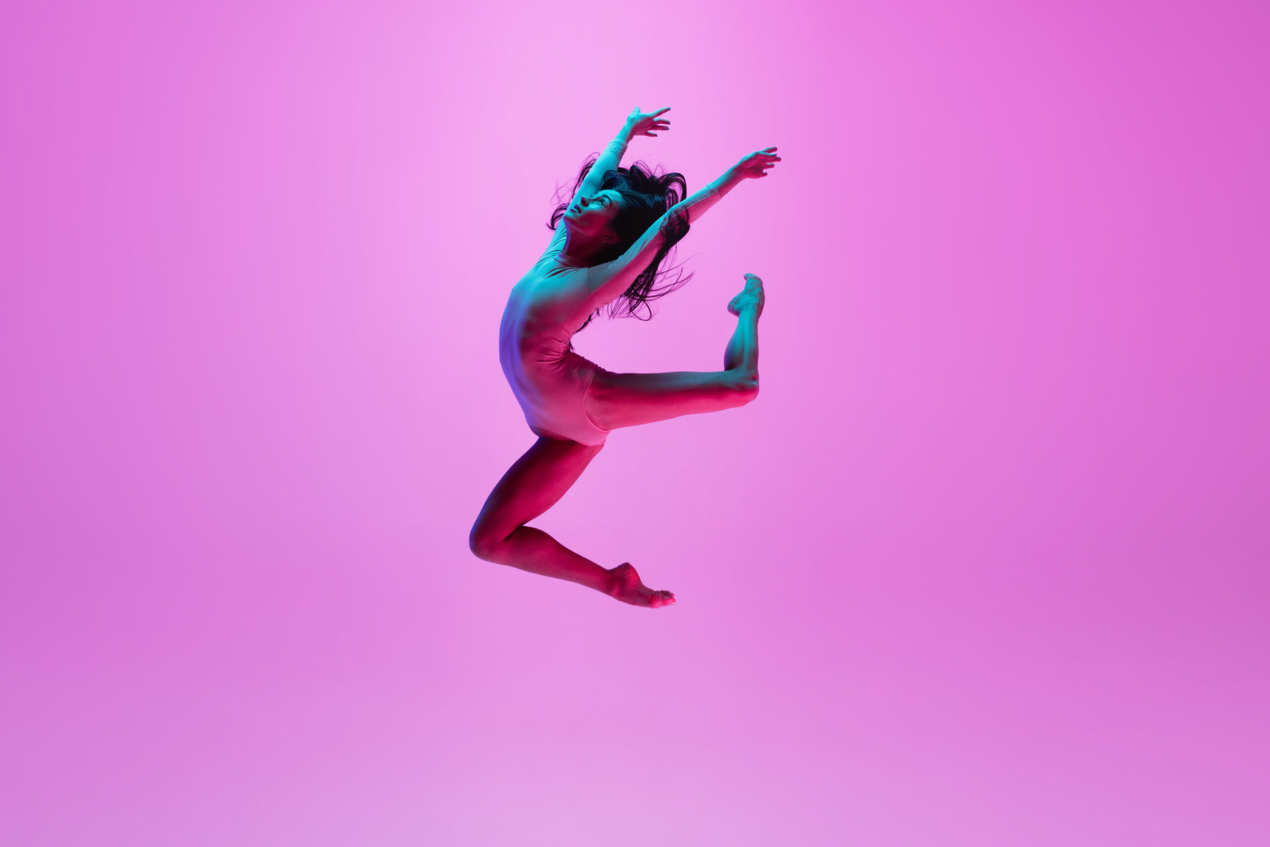 Young and graceful ballet dancer isolated on pink studio background in neon light. Art, motion, action, flexibility, inspiration concept.